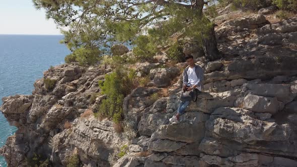 Aerial View of Young Man Traveler on Rock Cliff Against Sea.