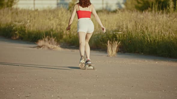Young Woman with Nice Legs Riding Skateboard on a Background of the High Grass