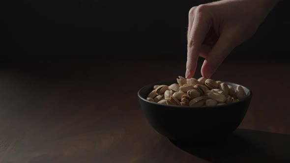 Slow Motion Man Take Roasted Pistachios From Black Bowl on Walnut Table