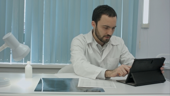 Serious Young Bearded Doctor Uses His Digital Tablet.