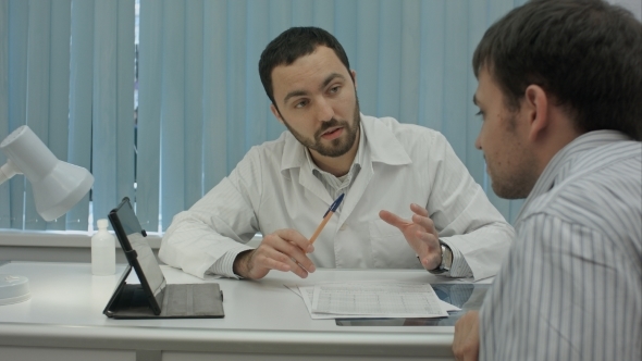 Male Bearded Doctor In Clinic Gives Reccomendations To Client.