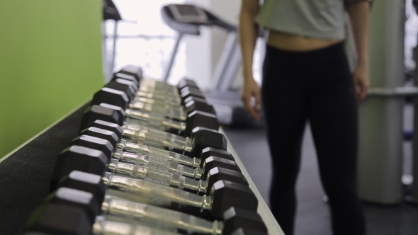 Athlete Woman Chooses Dumbbells With a Shelf In Gym.
