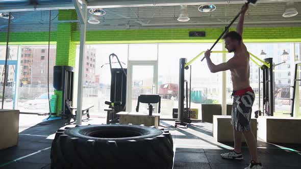 A Man Hits a Hammer on a Large Tire in the Gym