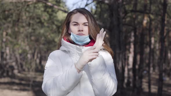Confident Caucasian Woman Putting on Protective Gloves and Face Mask. Portrait of Young Brunette