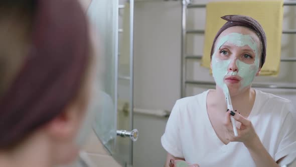 Woman Applying Mask Moisturizer for Skin on Face Looking in Mirror in Bathroom Spbas
