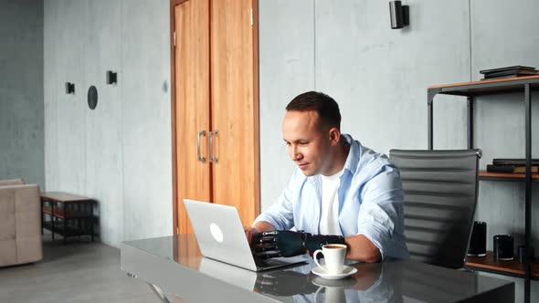 Disabled man with high temple and bio prothesis types on grey laptop