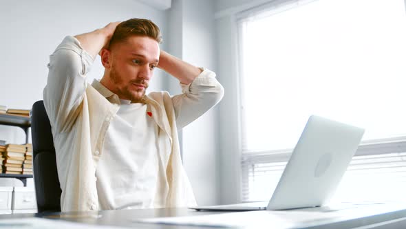 Depressed guy in yellow shirt looks at laptop