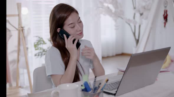 Business Asian woman Talk to work on the phone and take notes on the laptop with work from home.