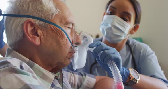 Video of biracial female doctor in face mask keeping oxygen to caucasian senior man