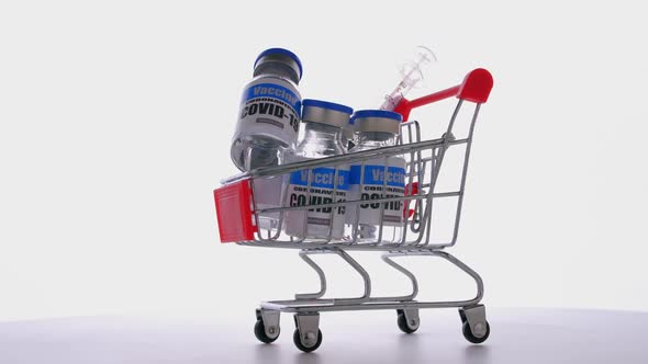 Glass vials for Covid-19 vaccine in shopping cart on white background. alt