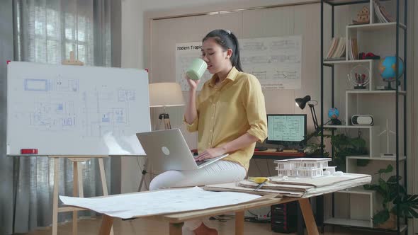 Woman Engineer Sitting On The Table And Drinking Coffee While Using A Laptop To Work At The Office