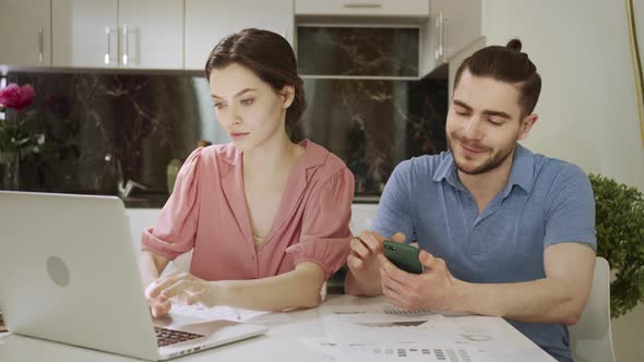 A Young Man is Searching Through the Internet While His Wife is Working at Home