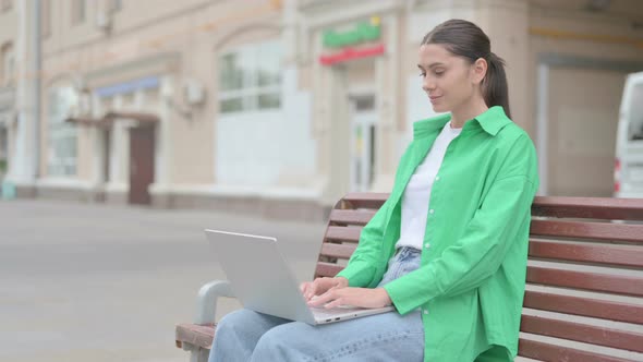 Hispanic Woman with Laptop Smiling at Camera While Sitting Outdoor on Bench