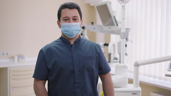 Medium Shot Smiling Positive Male Middle Eastern Dentist in Face Mask Crossing Hands in Slow Motion