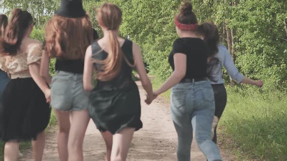 A Group of Girls Run Along the Village Road By the Forest Holding Hands