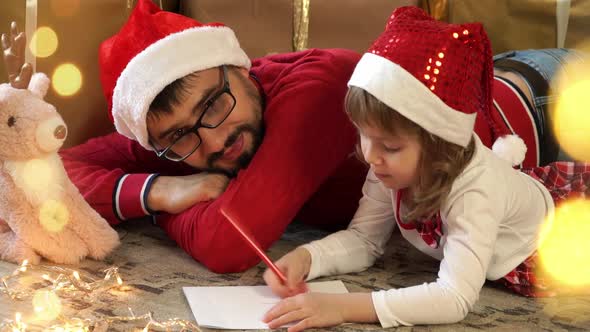 Father and Little Girl Write Letter to Santa Claus on Background of Christmas Boxes