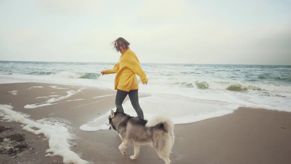 Young Beautiful Female Walking with Siberian Husky Dog on the Beach