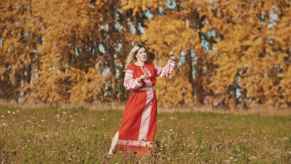 Woman in Red Traditional Dress Standing on the Field with a Sword and Talking with Cameraman