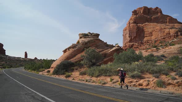 Hitchhiker Walks Along Road In Arches National Park
