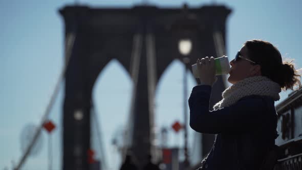 A Young Woman Is Enjoying A Hot Drink On A Cool Day On The Brooklyn Bridge