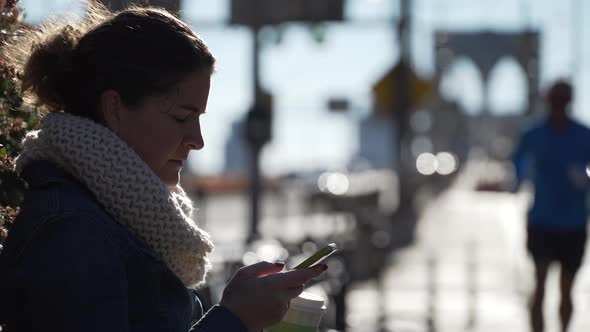 A Young Woman Is Looking At Her Phone Near The Brooklyn Bridge