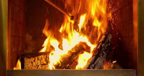 A Person Straightens a Log in the Fireplace with a Poker