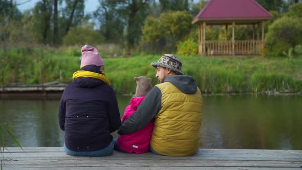 Rear View of Family Sitting on Pier in Autumn Day