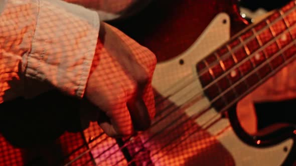 Close Up Man Playing Bass Guitar with His Finger in the Club with Neon Lights.