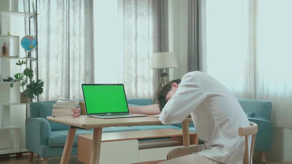 Side View Of Asian Man Student Being Sleepy While Looking At Green Screen Computer At Home