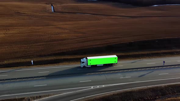 Truck with green screen on trailer drives along the highway in the rays of the setting sun.