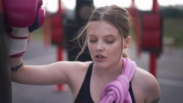 Perspiring Beautiful Woman in Boxing Gloves Rubbing Sweat Off Forehead Looking Away