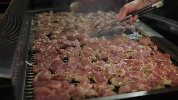 Chef is flipping meat on grill. Barbecue meat preparing on grill, close up