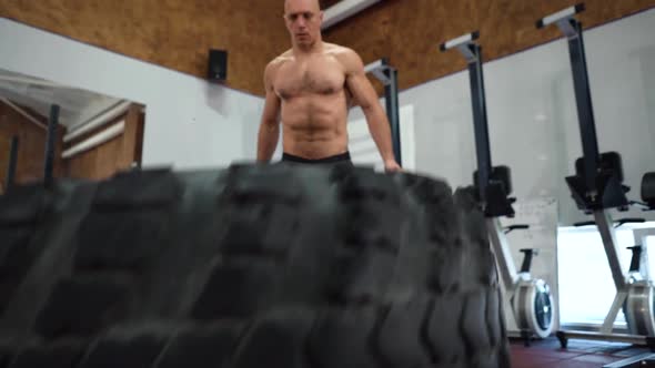 Strong muscular man lifts tire, crossfit training