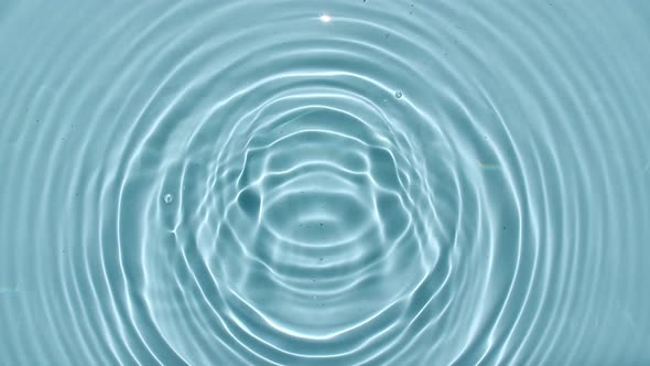 Top View Slow Motion of Drop Falls Into Water and Diverging Circles of Water on Blue Background