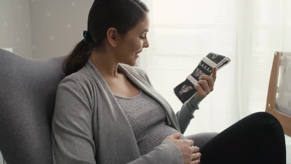 Close up video of caucasian woman in advanced pregnancy browsing ultrasound scan in baby's room.