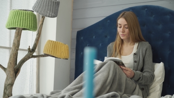 Attractive Woman  Reading a Book Sitting in Bed.