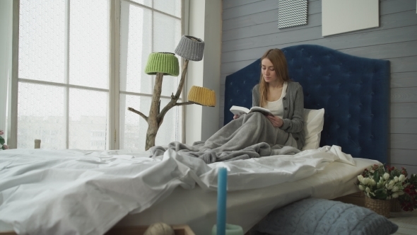 Young Woman Reading a Book While Sitting In Bed.