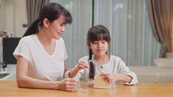 Asian Loving Mother teach young child daughter put coins in piggy bank to save money for future.