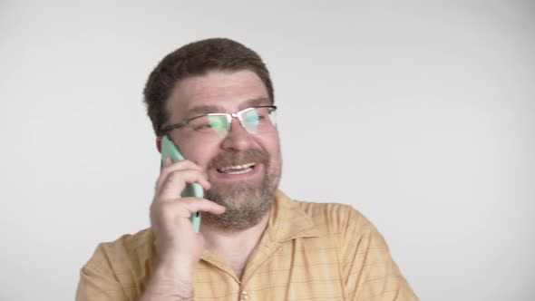 Man with a beard and glasses is happily talking on a smartphone on a gray background