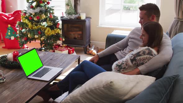 Caucasian couple looking at laptop with green screen sitting on the couch at home