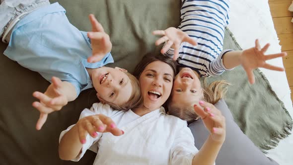 Happy Mother with Two Children Laying on Bed at Home Having Fun and Playing