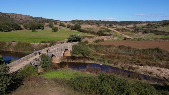 People walking over roman bridge Idanha a Velha, Portugal. Aerial forward