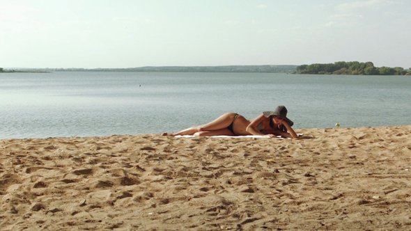 Woman In Hat With Sunglasses Reading At The Sand