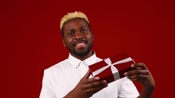 Latin Hispanic Man in White Tshirt in Red Studio Background with Small Gifts Box