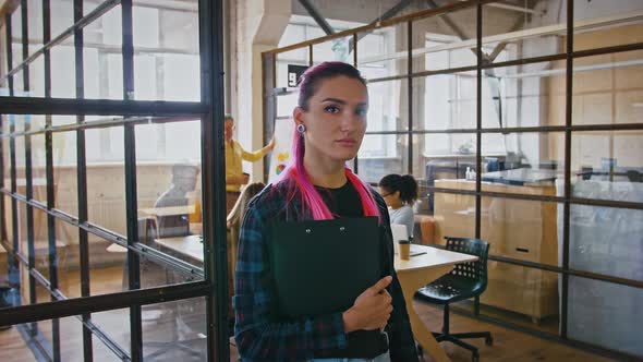 Portrait of Young Lady with Pink Hair Standing with Folder in Office During Team Meeting Tracking