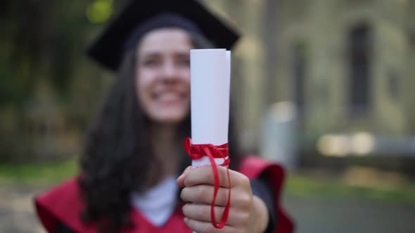 Closeup Diploma with Red Ribbon in Female Hand with Blurred Smiling Young Woman at Background