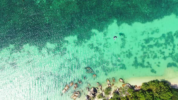 Parasol flying over beautiful sea with turquoise lagoon full of coral reef patterns on white sandy s