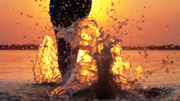 Silhouette of Legs of Boy Running Into the Water at Sunset and Creating Splashes. Slow Motion