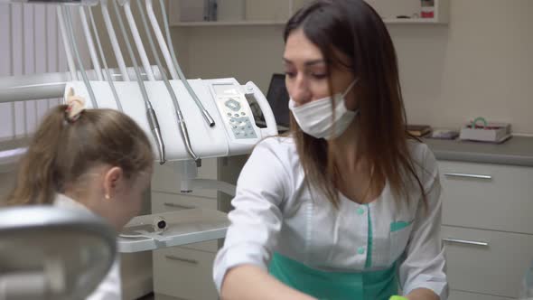 Friendly Female Dentist Taking Off a Napking After Procedures and Giving Cute Little Girl a
