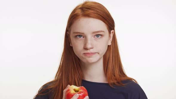 Concentrated Redhaired Teenage Caucasian Girl Eating Apple Chewing Fast on White Background